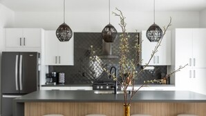 Een moderne keuken met een centraal eiland, witte kasten en hanglampen.