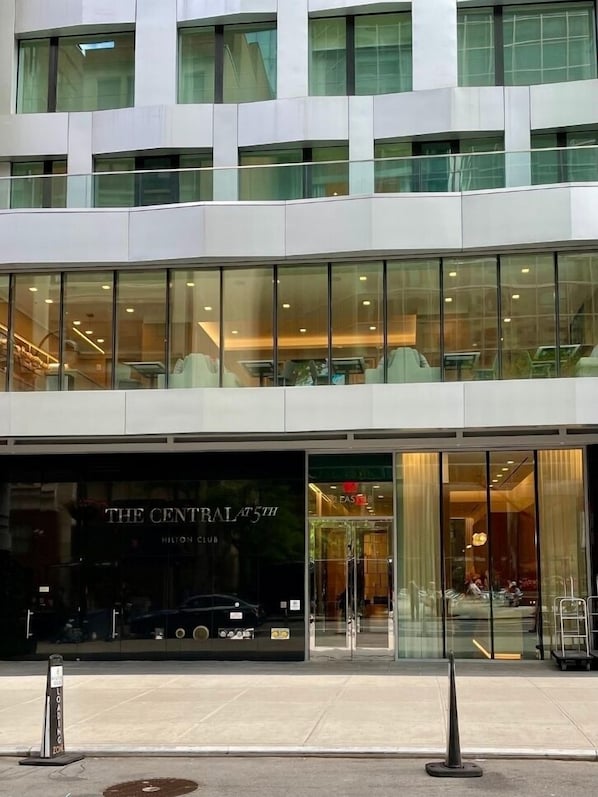 Un hôtel moderne doté d’une façade en verre, d’un restaurant bien visible appelé « The Central at 5th », et d’une enseigne « Hilton Club ».