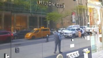 A glass facade of The Central at 5th Hilton Club with reflections of vehicles and a person on the ground.