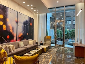 Un salon moderne avec un canapé, un fauteuil et une table basse, de grandes peintures abstraites et une vue sur la ville grâce à de grandes fenêtres.