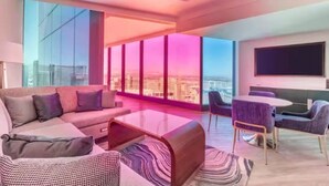 A modern living room with a sofa, coffee table, and chairs, large windows with a city view, and a flat-screen TV mounted on the wall. - Las Vegas | Luxury City Retreat | Pool + Gym | 2BR (Las Vegas)