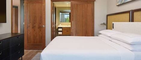 Habitación de hotel con cama, cómoda, espejo y puerta que da a un baño.