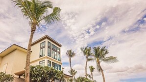 A two-story building with a modern design, surrounded by palm trees and a partly cloudy sky.