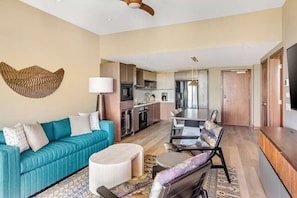 A modern living room with a sofa, ottoman, and a dining area with a table and chairs. - Maui | Upscale Island Escape | Pool + Beach Access (Kihei)