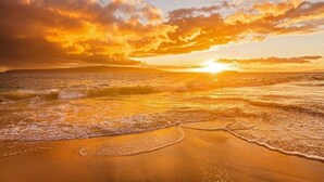 A beach with waves, a sunset, and a clear sky.