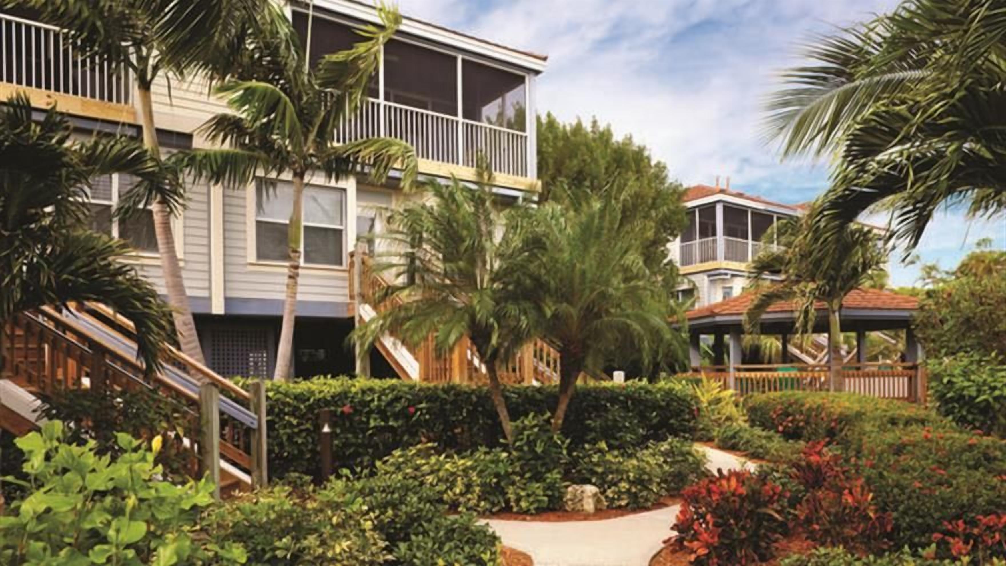 A multi-story building with balconies, surrounded by lush greenery and palm trees.