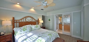 A bedroom with a bed, bedside lamps, a ceiling fan, and a door leading to another room.