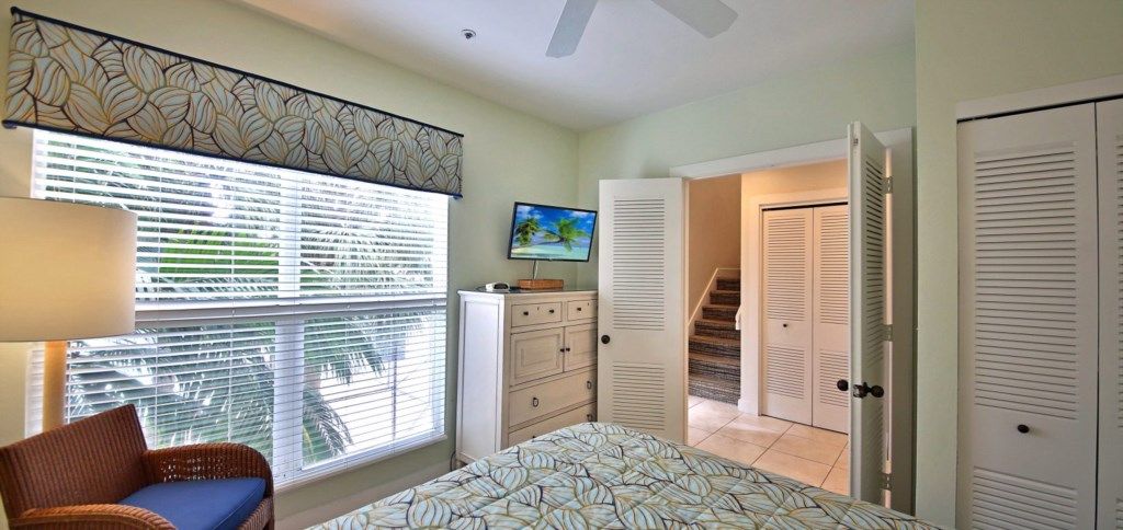 A bedroom with a bed, a dresser, a television, and a staircase leading to a closet.
