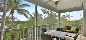 Un espace extérieur abrité, doté d’une table et de chaises, d’un coin salon confortable et offrant une vue sur des palmiers et une végétation luxuriante.