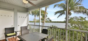 A balcony with a table and chairs, overlooking a body of water and palm trees.