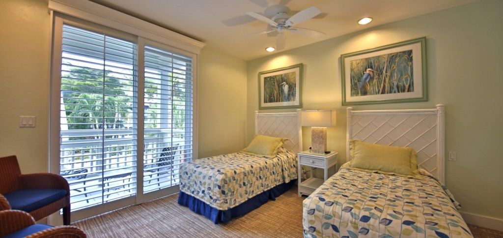 A hotel room with two beds, a chair, a desk, and a window with blinds.