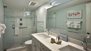 A modern bathroom with a glass-enclosed shower, a large mirror, and a white sink with toiletries.