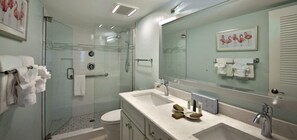 Un baño moderno con ducha de vidrio, un espejo grande y un lavamanos blanco.