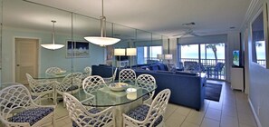 A modern living room with a glass dining table, white wicker chairs, and a blue sofa.