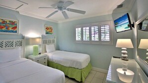 A hotel room with two beds, a ceiling fan, a TV, and artwork on the walls.