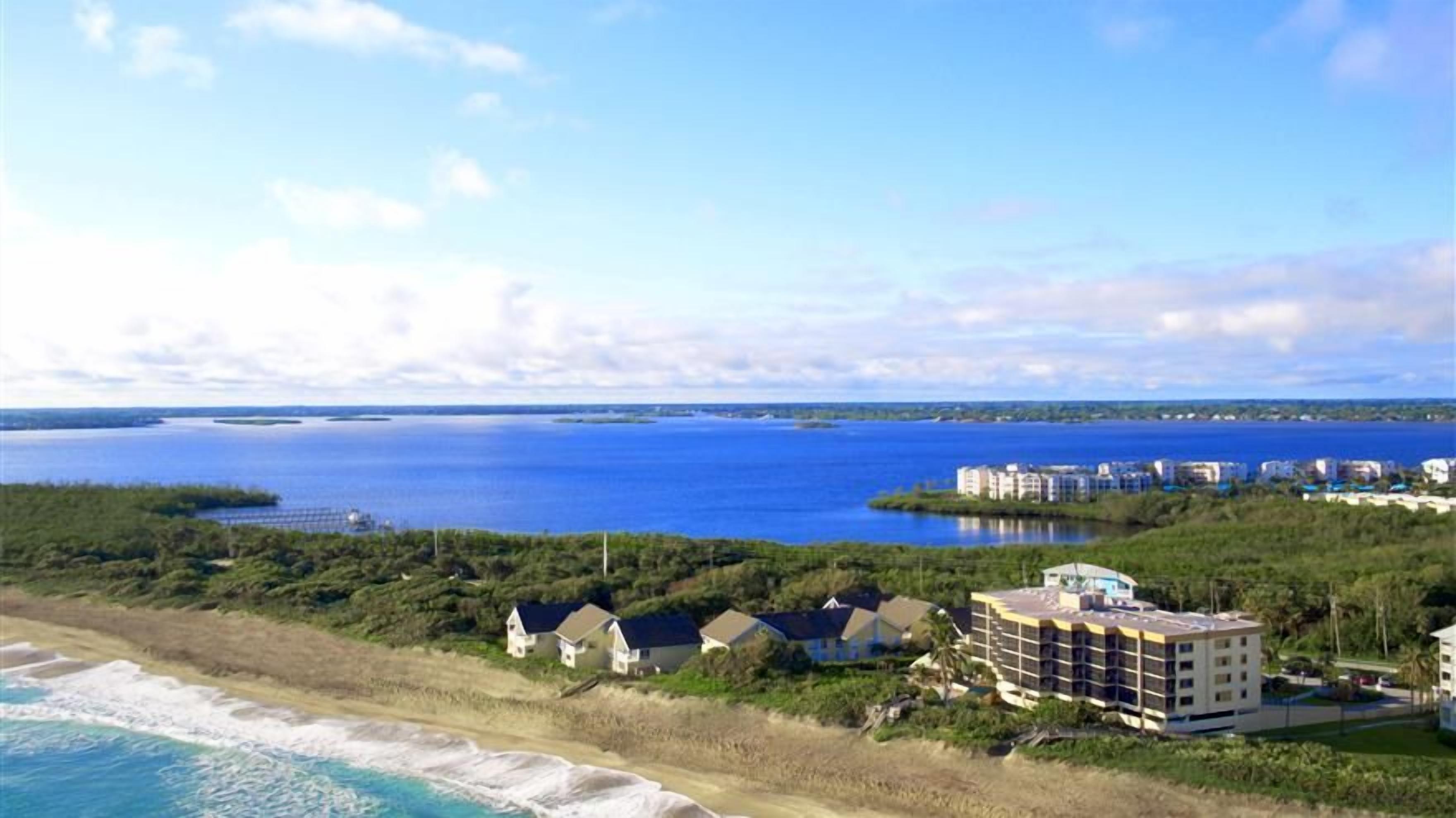 A coastal hotel with multiple buildings, a beach, and a large body of water.