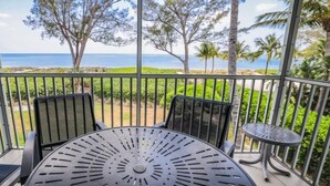 A balcony with a table and chairs, overlooking a beach and palm trees.