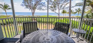 Un balcón con mesa y sillas, con vista a una playa y palmeras.