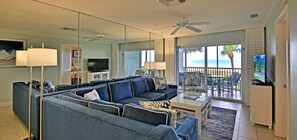 A living room with a sofa set, a coffee table, a TV, and a balcony with a view of the ocean.