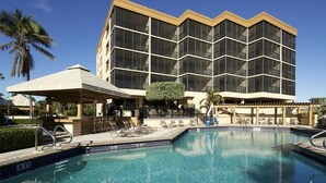 A hotel with a large pool, a covered seating area, and a modern building facade.