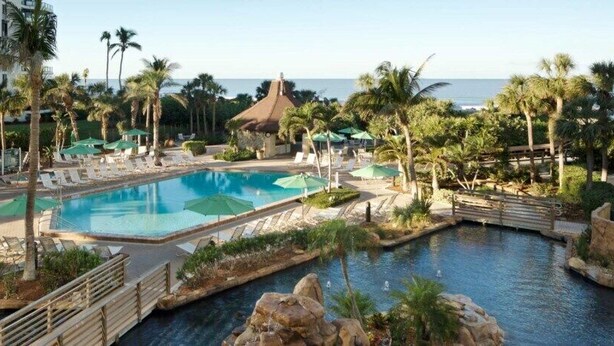 A resort pool area with multiple pools, lounge chairs, and palm trees.