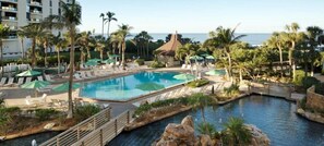 Un espace piscine dans un complexe hôtelier, comprenant plusieurs piscines, des chaises longues et des palmiers.