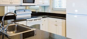 Une cuisine moderne dotée d’appareils électroménagers en acier inoxydable, de meubles blancs et d’un plan de travail en granit noir.