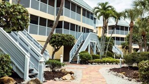 A hotel with a central staircase, palm trees, and a paved walkway.