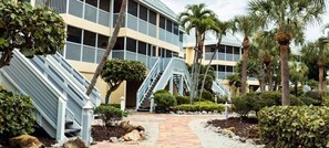 Un hotel con una escalera central, palmeras y un camino pavimentado.