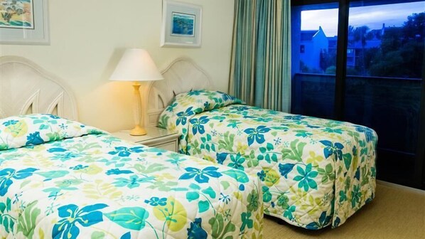 Una habitación de hotel con dos camas, una mesita de noche con lámpara y una ventana con cortinas.