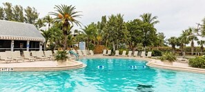 Una piscina con sillones de descanso y palmeras.