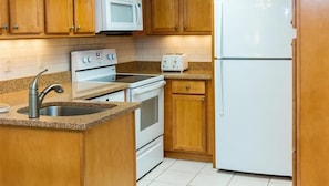 Una cocina con armarios de madera, microondas blanco, estufa, tostadora y refrigerador.