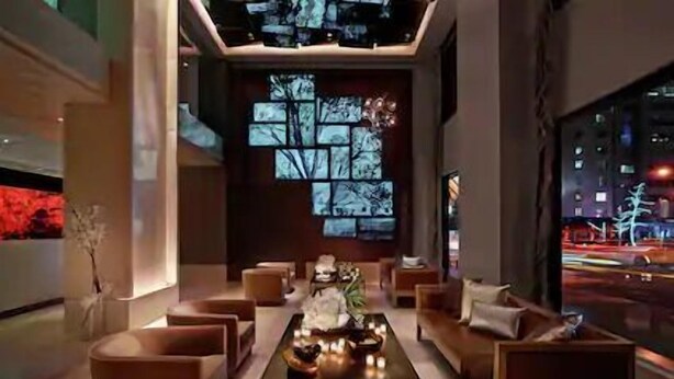 A modern interior with a central coffee table, sofas, and a wall with a tree projection. - NYC | Midtown Location | Central Park | 1BR Premier+ (New York)
