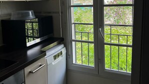 A kitchen with white cabinets, a black countertop, a dishwasher, and a window with a view of a garden and a building.