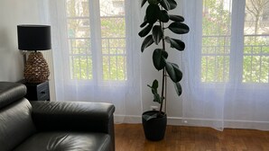 A living room with a black leather sofa, a colorful rug, a potted plant, and a lamp on a side table.