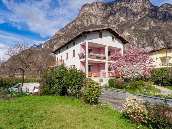 Un immeuble à plusieurs étages doté de balcons, entouré d’une végétation luxuriante et de montagnes.