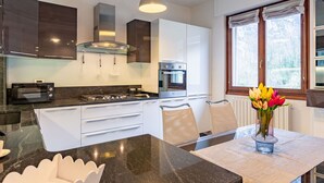 Eine moderne Küche mit weißen Schränken, einer schwarzen Arbeitsplatte und einem eingebauten Backofen. Ein Fenster mit Vorhängen und ein Blumenstrauß auf dem Tisch sind zu sehen.