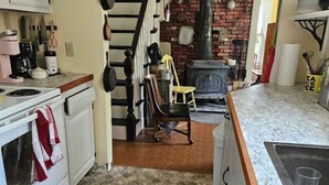 A kitchen with a stove, sink, and a dining area with a chair and table. - Perry Shore Road Cottage (Perry)