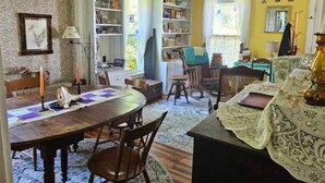 A cozy living room with a dining area, featuring a round table, chairs, a bookshelf, and a window with curtains. - Perry Shore Road Cottage (Perry)