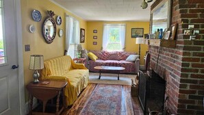 A cozy living room with a yellow sofa, a patterned armchair, a coffee table, and a fireplace. - Perry Shore Road Cottage (Perry)