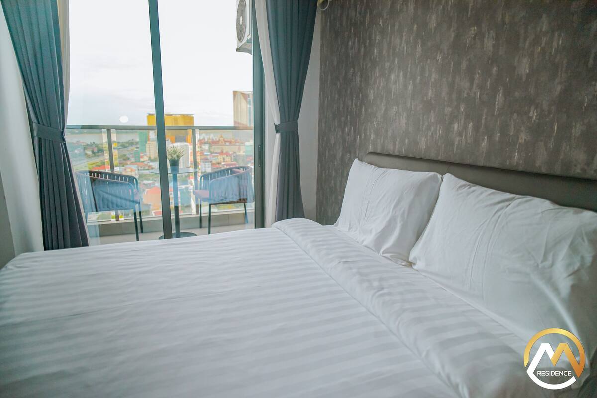 Habitación de hotel con una cama grande, vistas de la ciudad desde un balcón y un diseño moderno.