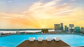 Una piscina con sillones de descanso y un horizonte urbano al fondo.