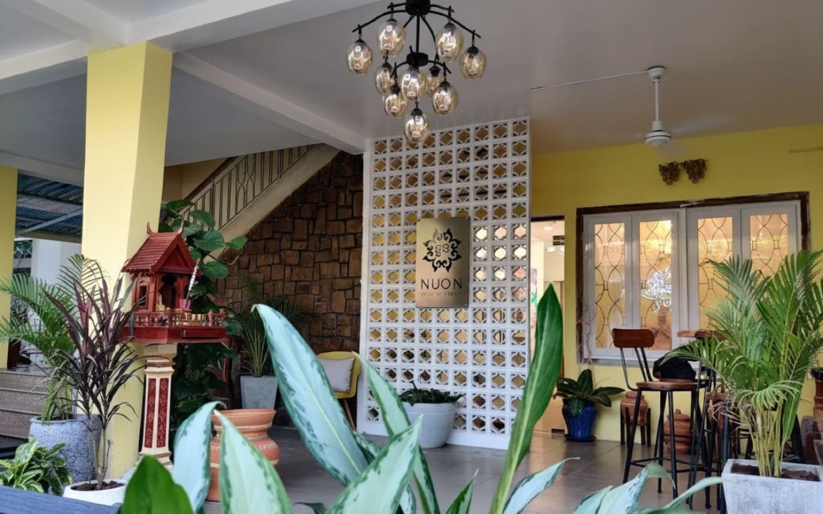 A hotel lobby with a staircase, a decorative wall with a sign, and various potted plants.