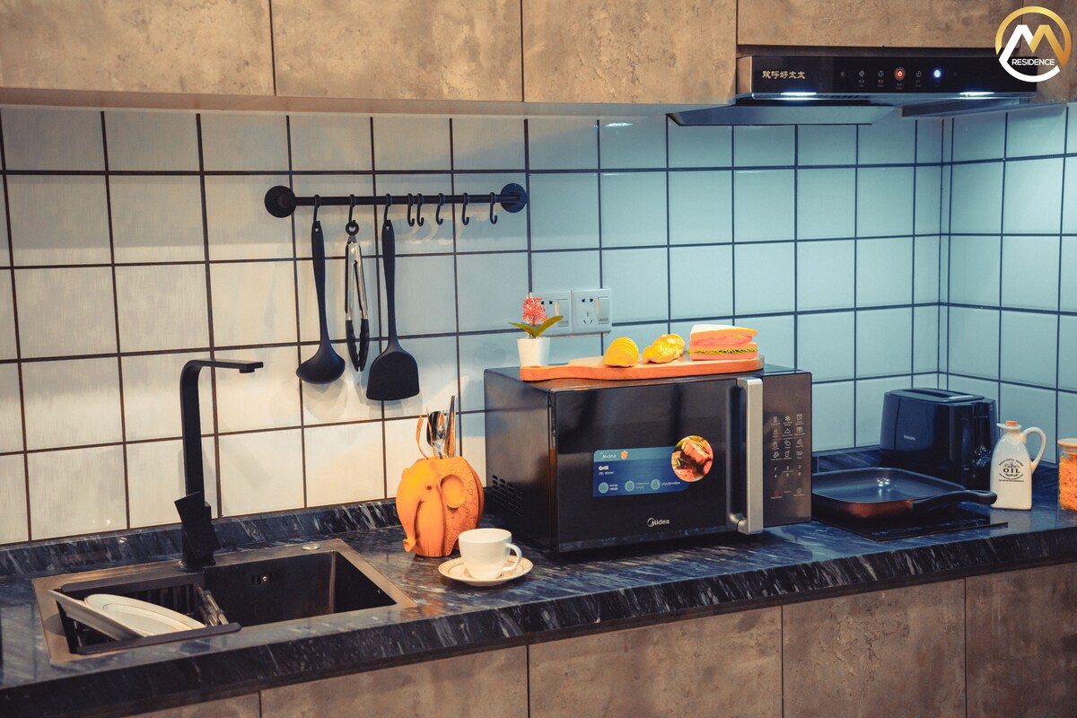 Una cocina moderna con encimera negra, horno empotrado, cafetera y tostadora.
