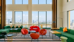 Un salón amplio con ventanas grandes, sofás verdes, sillas rojas y vista a la ciudad.