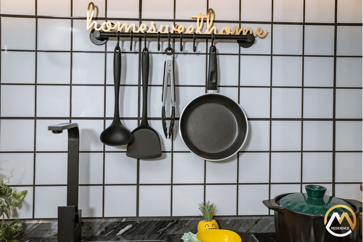 Een keuken met een zwart-wit betegelde spatwand, een hangende kruidenrek met keukengerei, en een groene pot op het aanrecht.