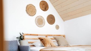 Une chambre avec un lit en bois, un canapé gris et des œuvres d’art murales en fibres tressées.