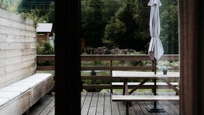 Une terrasse en bois avec un banc et une table de pique-nique, donnant sur une zone boisée.