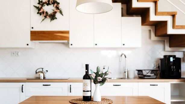 Une cuisine moderne avec des meubles blancs, un escalier en bois et un luminaire suspendu.