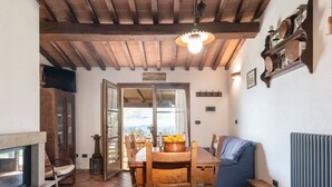 A rustic dining area with a wooden table and chairs, a fireplace, and a view through an open door. - Beautiful private villa for 5 people with WIFI, TV, terrace and panoramic view (Roccastrada)